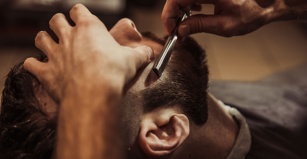 Barber using a straight razor to shape a customer's beard